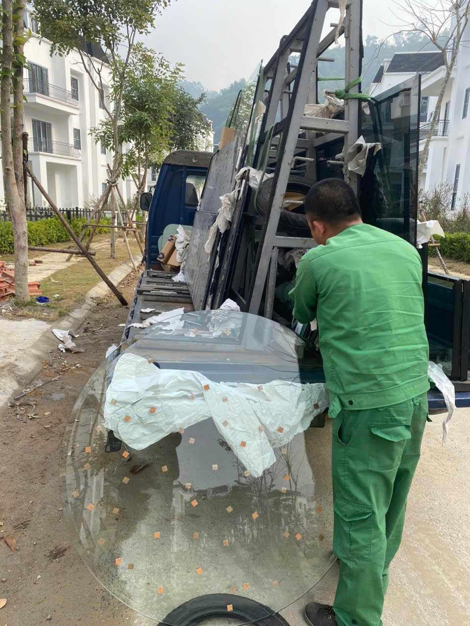 Công nhân đang vận chuyển tấm kính cường lực lớn từ thùng xe tải tại công trình xây dựng